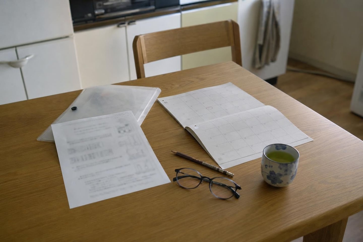 a kitchen table with a school printout, a calendar with one date circled, glasses and a cup of tea